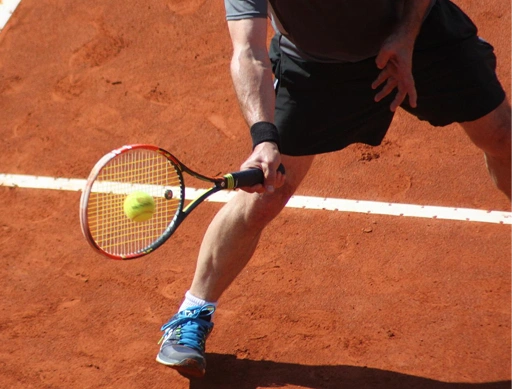 Joueur de tennis frappant une balle basse sur un court en terre battue.